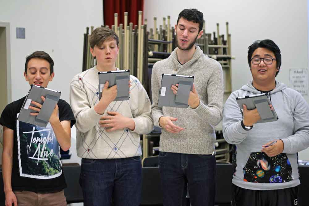 Singers rehearsing together, each following their part on a tablet